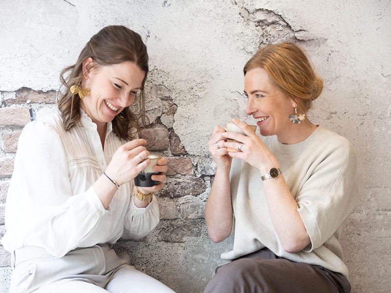 Twee medewerkers van Nieuwenhuis Makelaardij ontspannen in gesprek met koffie op kantoor